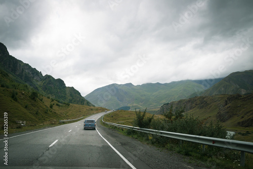 Small old stylish car is moving along the mountain highway. Scenic view on the road with majestic mountains on sides. © Sergey_T
