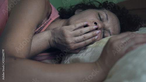 Young woman lying in bed awakening and yawning from a sleep stretching