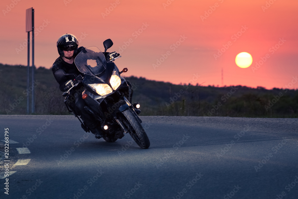 Obraz premium sylwetka jeźdźca na motocyklu jazdy o zachodzie słońca - miejsce na tekst