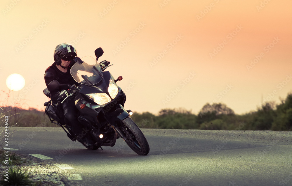 Fototapeta silhouette of rider on a motorbike driving at sunset - space for your text
