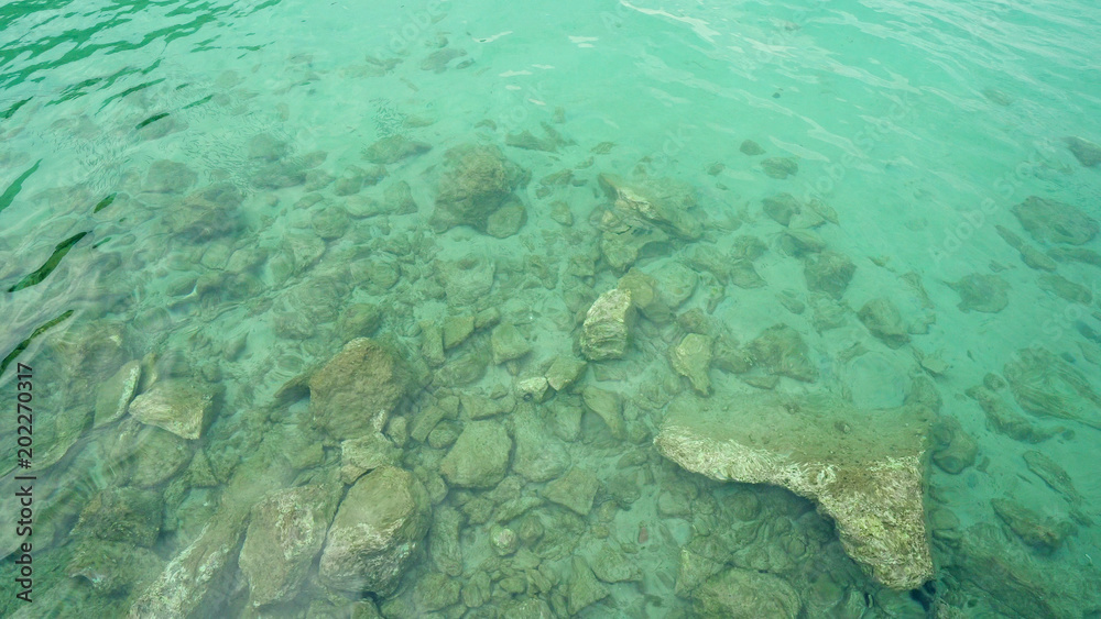 Turquoise shallow water surface and rocks stones on sea floor