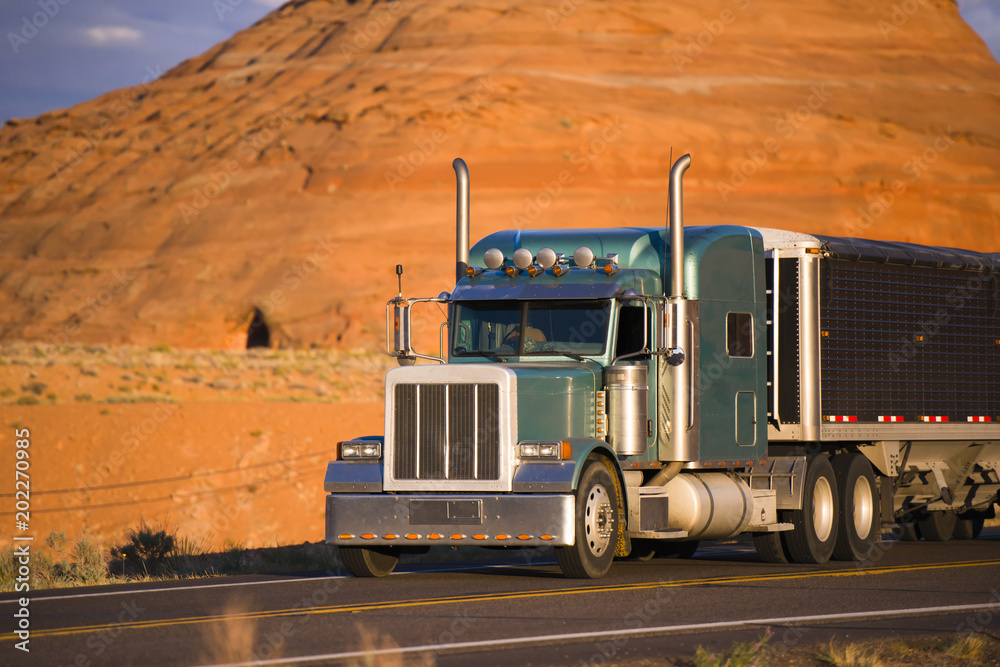 Classic big rig semi truck with low bulk covered semi trailer transporting cargo on the road in Page Arizona Classic big rig semi truck with low bulk covered semi trailer transporting cargo on the road in Page Arizona