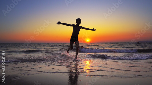 Boy child is running out of water on a sea beach at sunset  cinematic steadicam shot