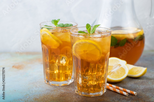 Traditional iced tea with lemon, mint and ice in tall glasses. Two glasses with cool summer drink on old rusty background