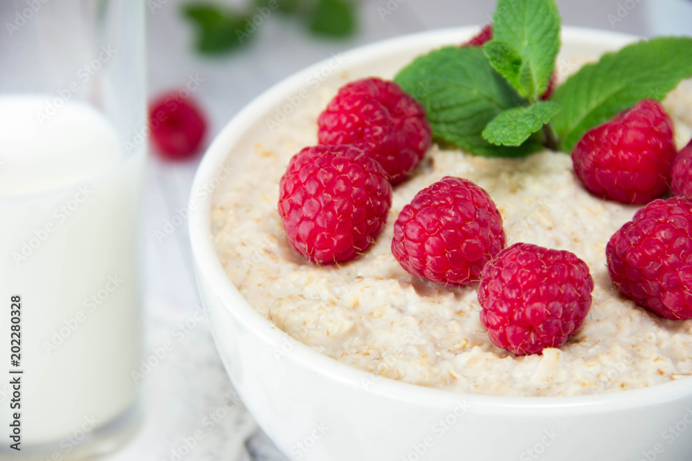 fresh delicious oatmeal with raspberries and mint, next to a mug with milk, a healthy diet, a nutritious breakfast