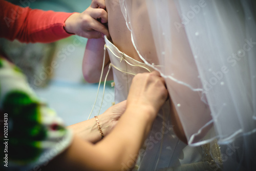 Hands of helper who helps bride to dress white wedding dress