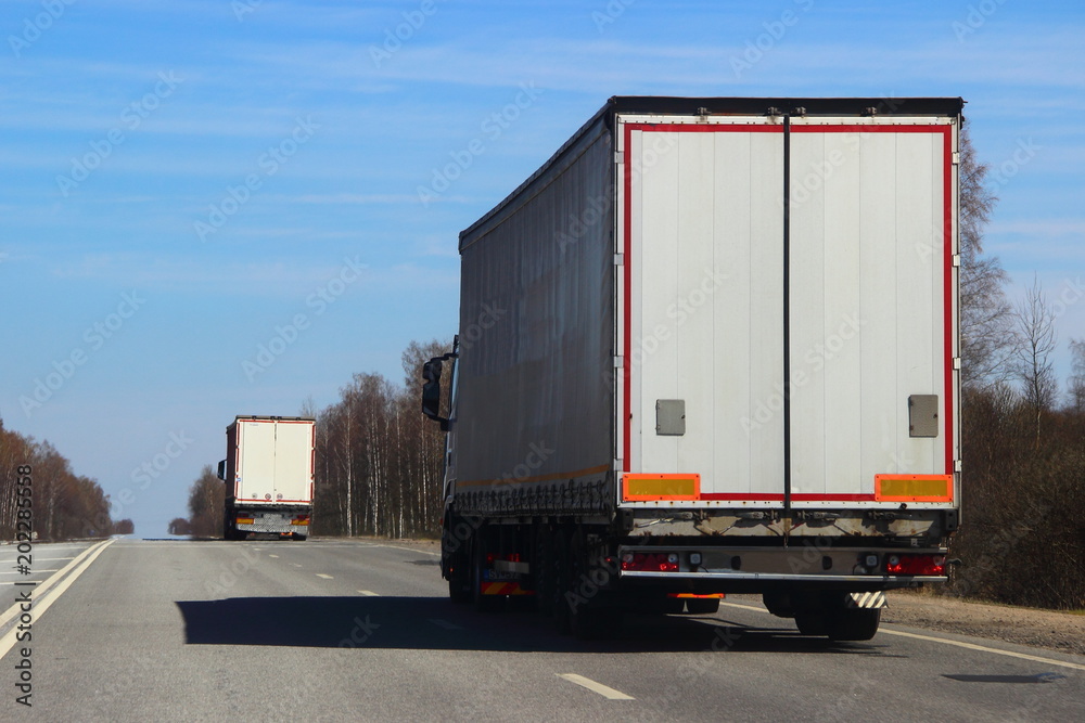 Transportation logistics - white semi trailer truck on asphalt road in summer on blue sky background, rear view Transportation logistics - white semi trailer truck on asphalt road in summer on blue sky background, rear view