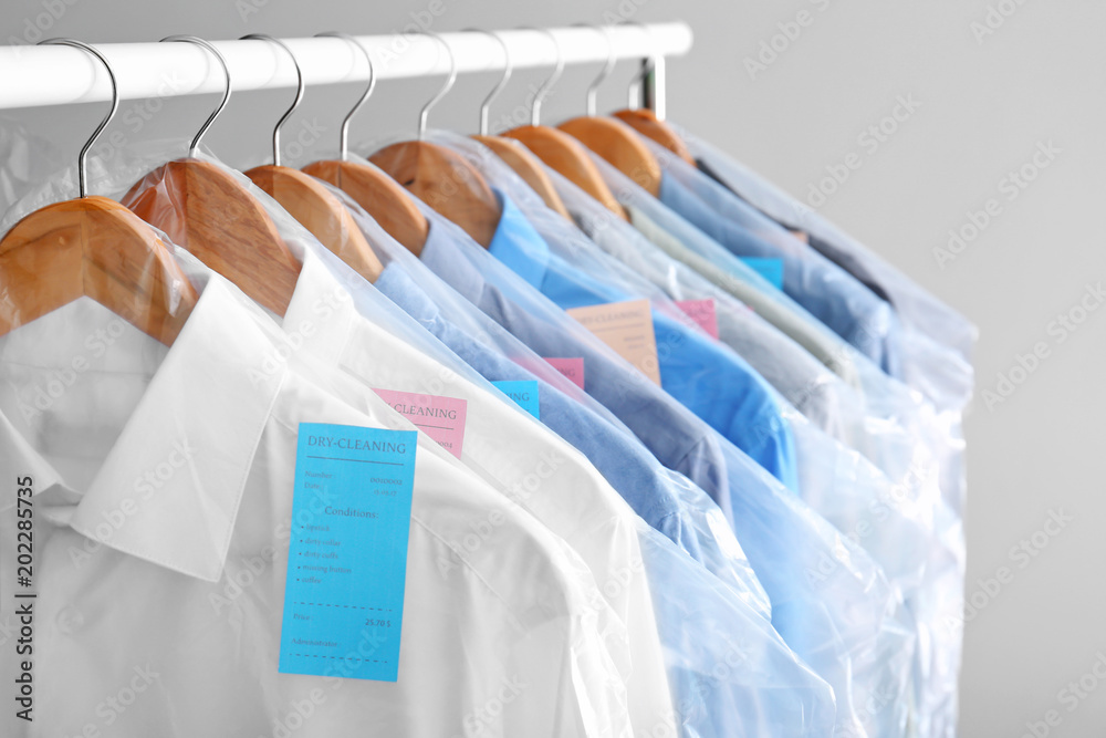 Rack with clean clothes on hangers after dry-cleaning against light  background Stock Photo | Adobe Stock