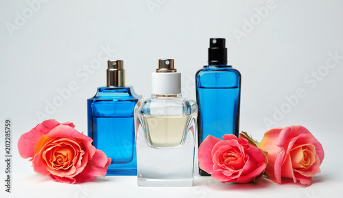 Composition with transparent bottles of perfume and beautiful flowers on white background