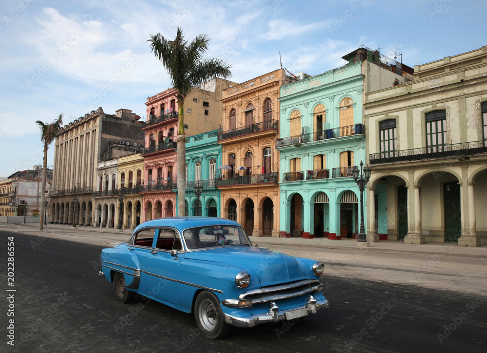 Colorful buildings and historic colonial archtiecture with a generic Classic car (logos & hood or bonnet ornament removed) on Paseo del Prado, downtown Havana, Cuba.