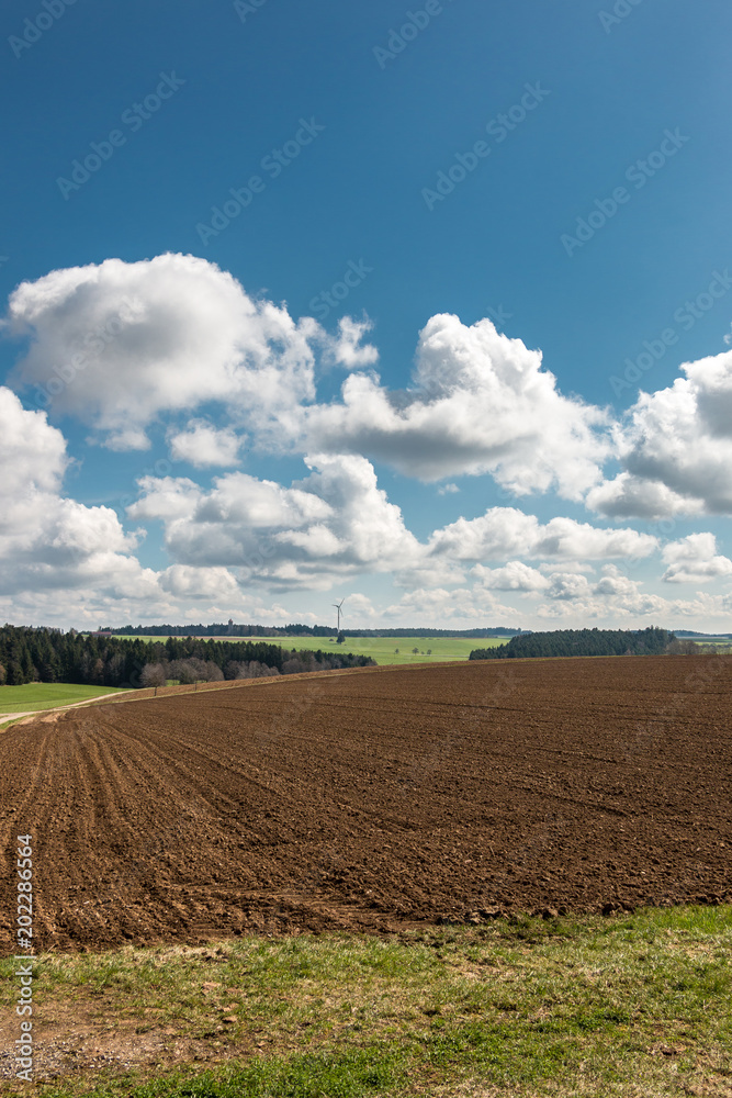 Big brown fields of fertile soil, green forest and wind power in the background Big brown fields of fertile soil, green forest and wind power in the background