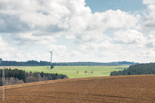 Big brown fields of fertile soil, green forest and wind power in the background