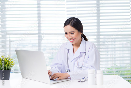 Young smiling female doctor sitting at office desk and working with a laptop