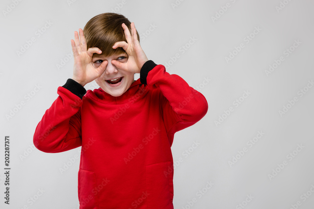 Cute confident little caucasian boy in red sweater fooling showing off on grey background Cute confident little caucasian boy in red sweater fooling showing off on grey background