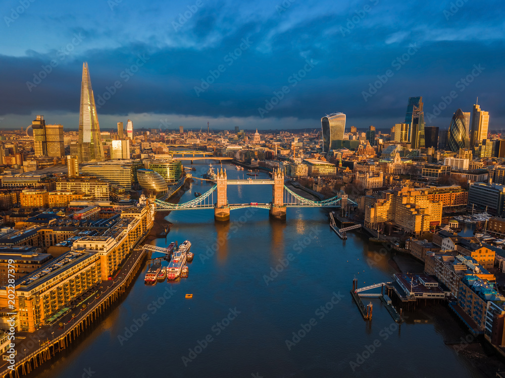 London, England - Aerial skyline view of London including iconic Tower Bridge with red double-decker bus, Tower of London, skyscrapers of Bank District at golden hour early in the morning
