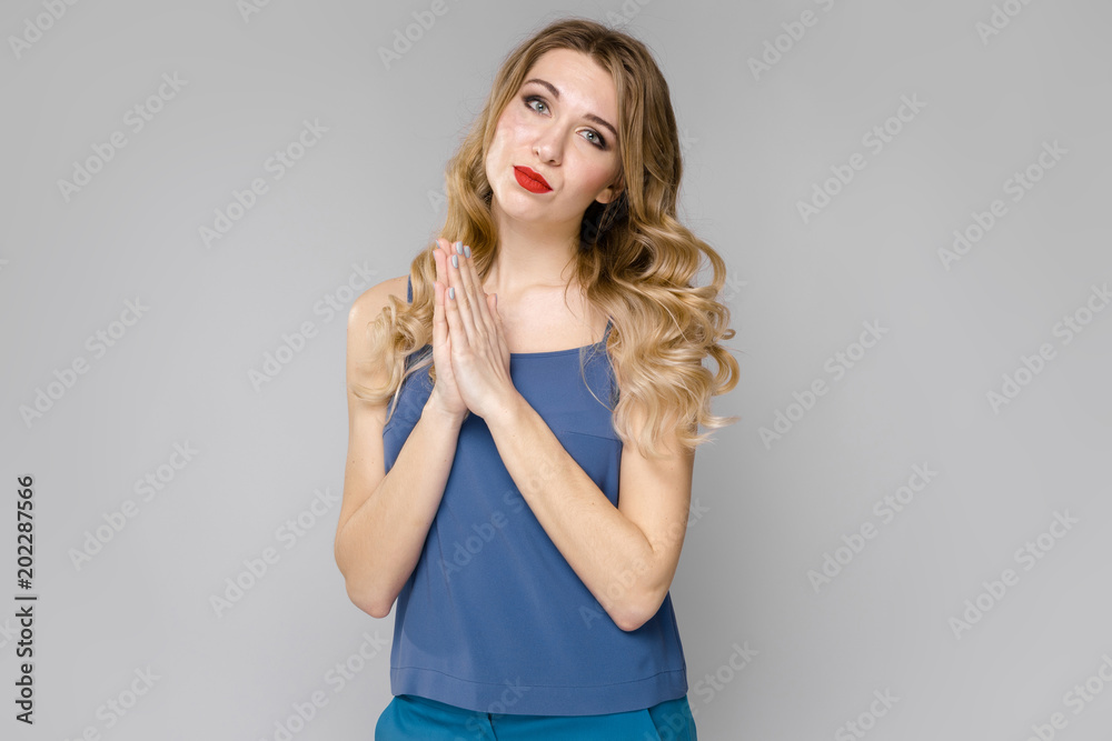 Charming young blonde upset girl in blue clothes showing hope gesture on gray background Charming young blonde upset girl in blue clothes showing hope gesture on gray background