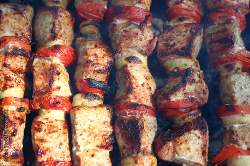 Pieces of juicy slices of marinated pork meat strung on skewers with slices of chopped tomatoes and onion cooking on barbecue. Cooking shashlik on the brazier