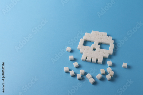 Skull of cubes of sugar and pieces of sugar on a blue background. Concept Sugar kills and harm sweet on the human body.