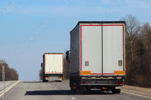 Transportation logistics - white semi trailer truck on asphalt road in summer on blue sky background, rear view
