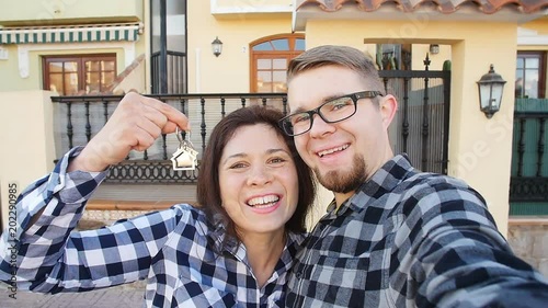 Young Couple with keys standing outside new home and taking a selfie photo