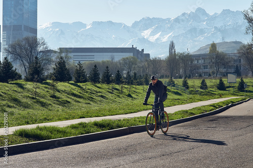A man with the black bicycle goes against the background of big mountains in the city of Almaty