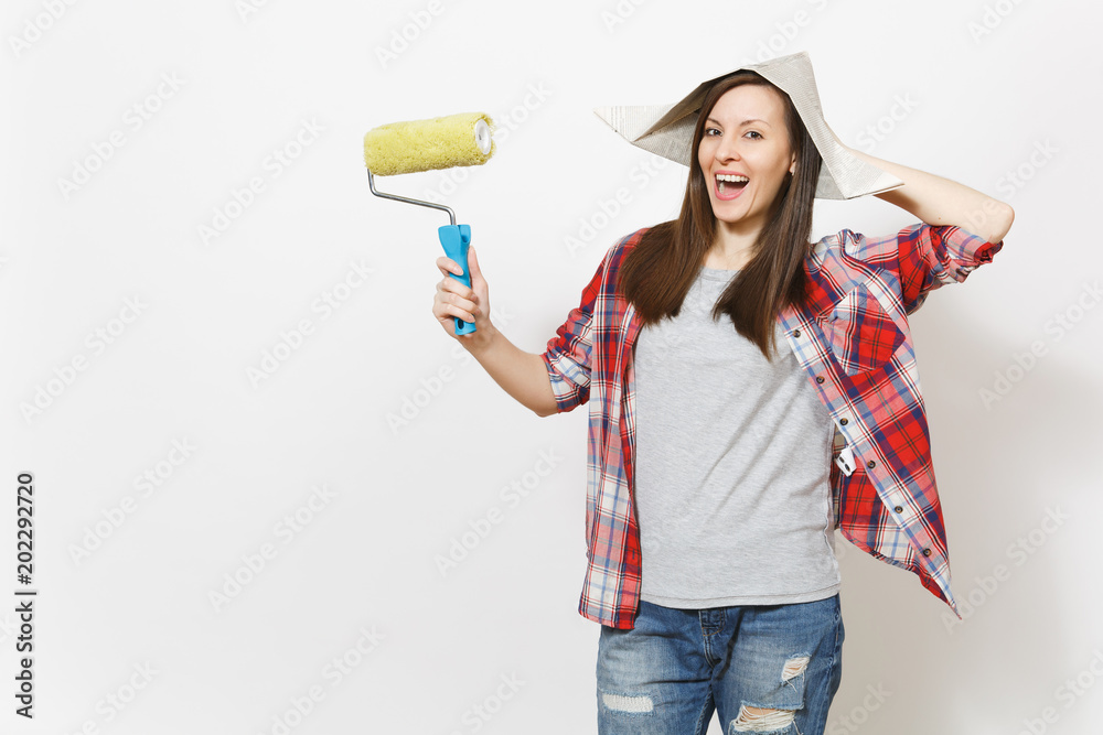 Young smiling beautiful woman in casual clothes and newspaper hat holding roller for wall painting isolated on white background. Instruments, tools for renovation apartment room. Repair home concept. Young smiling beautiful woman in casual clothes and newspaper hat holding roller for wall painting isolated on white background. Instruments, tools for renovation apartment room. Repair home concept.