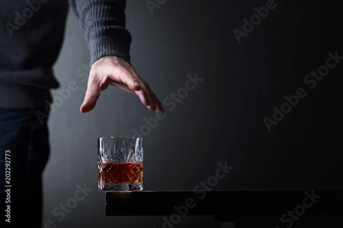 Man's hand reaches for a glass of alcohol.