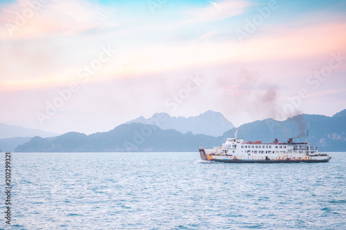 Beautiful sunset with mountain and ferry boat transporting passengers to island over horizon clam sea in evening background.