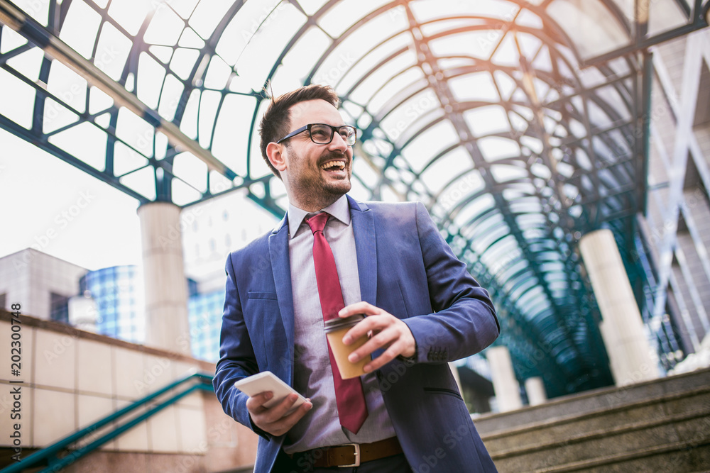 Businessman using mobile phone outside of office buildings in the background. Young caucasian man holding smartphone for business work and drink coffee to go. Businessman using mobile phone outside of office buildings in the background. Young caucasian man holding smartphone for business work and drink coffee to go.