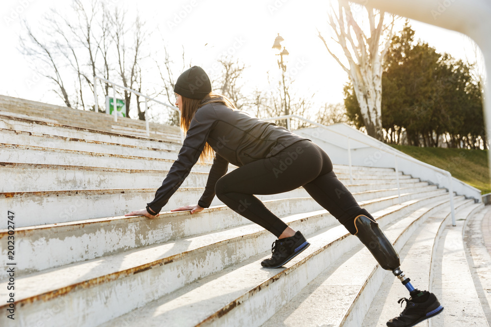 Image of disabled running girl with prosthetic leg in sportswear, exercising at the stairs outdoors