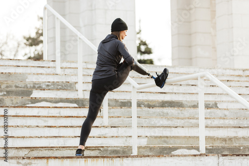 Image of disabled running girl in sportswear, training and stretching prosthetic leg in stadium outside