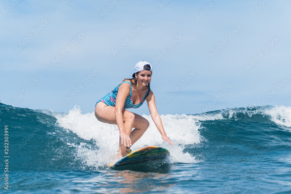 smiling woman in swimming suit surfing in ocean
