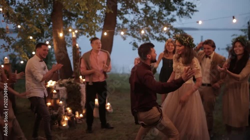 Cheerful illuminated bride shows guests dance open air