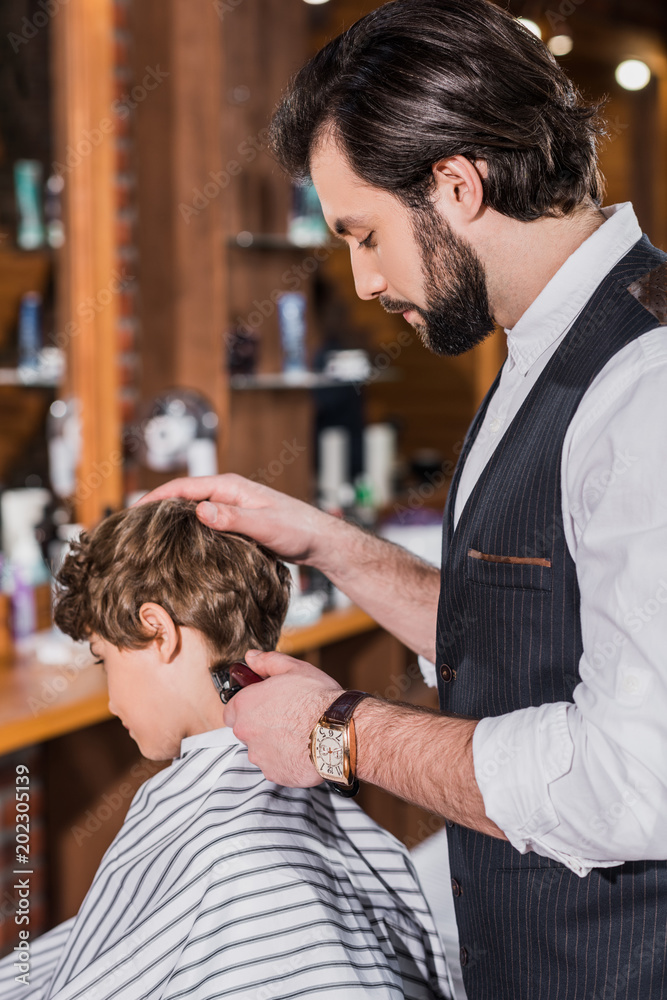 adorable curly kid getting haircut from barber with Hair Clipper adorable curly kid getting haircut from barber with Hair Clipper