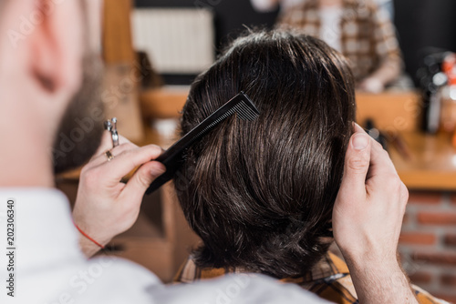 cropped shot of barber combing hair of customer at barbershop