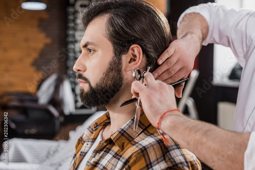 side view of bearded man getting haircut in barbershop