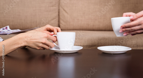 Side view photo of female hands hold a white cups of black coffee on table at home or cafe.