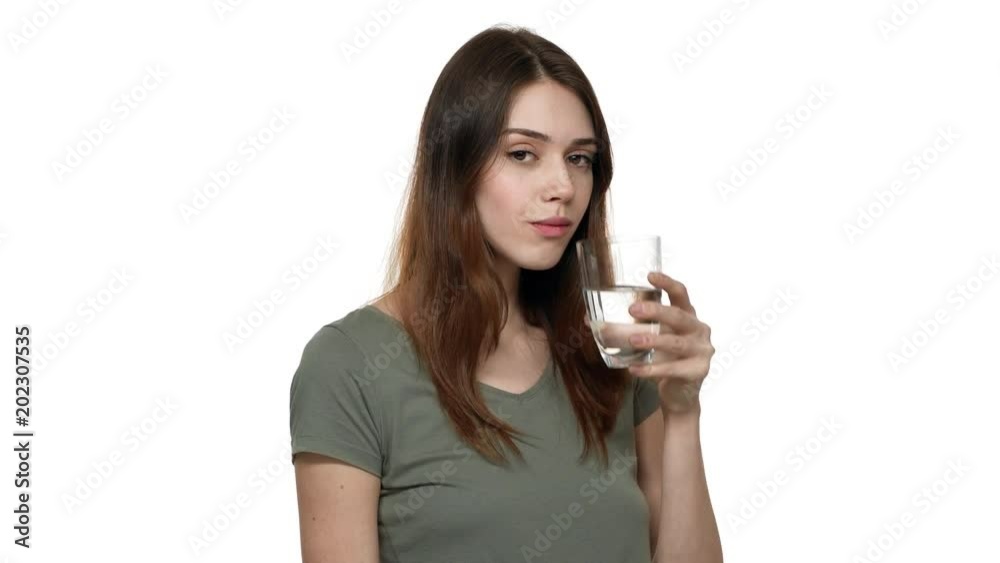Portrait of healthy woman with brown hair drinking fresh water from transparent glass and smiling on camera, over white background closeup. Concept of emotions Portrait of healthy woman with brown hair drinking fresh water from transparent glass and smiling on camera, over white background closeup. Concept of emotions
