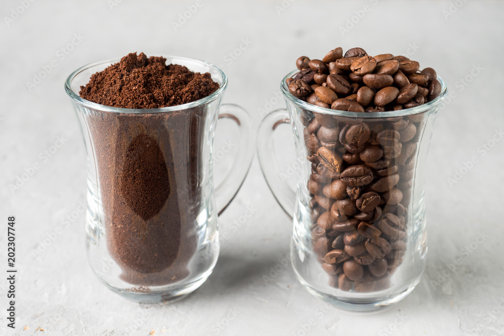 Two glass cups with coffee beans and ground coffee on light concrete background Two glass cups with coffee beans and ground coffee on light concrete background