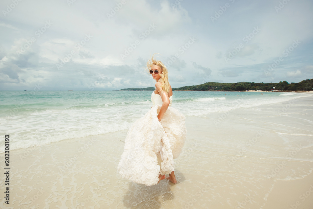 young woman in wedding dress goes over sea turning back. bride on the beach. young woman in wedding dress goes over sea turning back. bride on the beach.