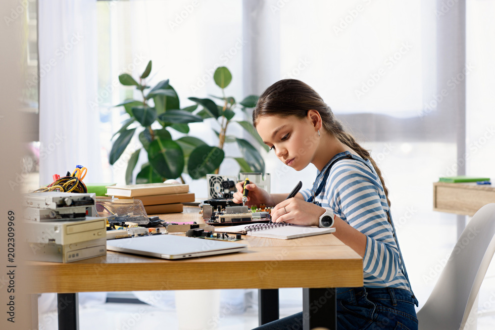 side view of adorable preteen child fixing computer motherboard and making notes at home side view of adorable preteen child fixing computer motherboard and making notes at home