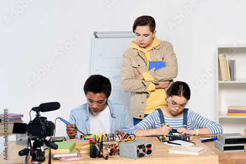 teen boy watching how multicultural friends soldering computer circuit with soldering iron at home