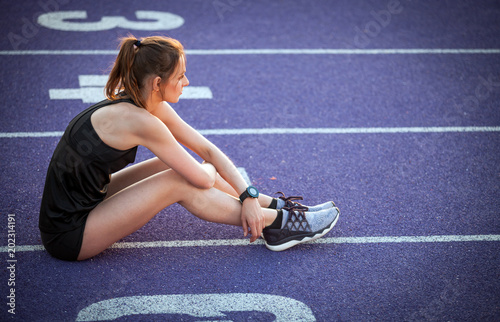 Athletic woman sitting on running track and resting after training