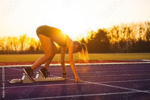 Fototapeta Naklejka Na Ścianę i Meble -  Athletic woman on running track starting from start line during sunset