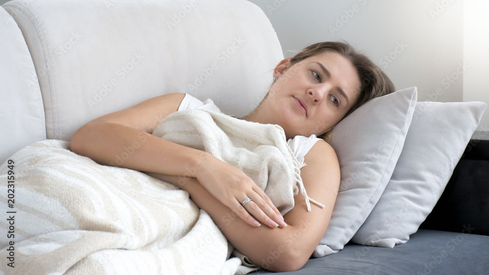 Portrait of young woman with depression lying on sofa under blanket Portrait of young woman with depression lying on sofa under blanket