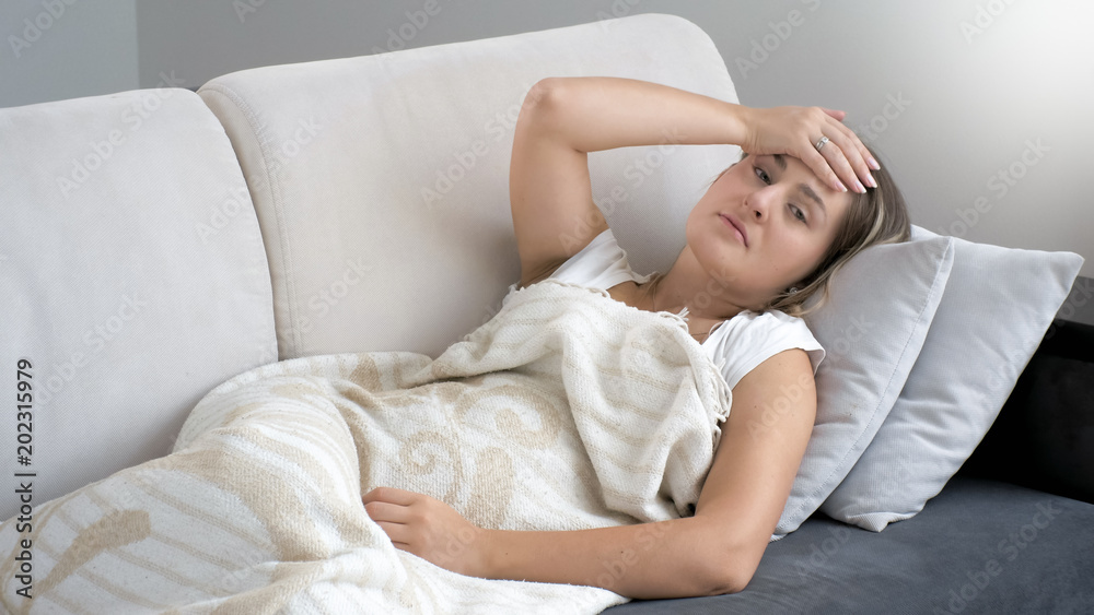 Portrait of young woman lying on sofa and feeling high temperature Portrait of young woman lying on sofa and feeling high temperature