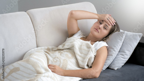 Portrait of young woman lying on sofa and feeling high temperature