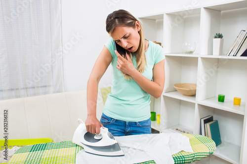 Busy and worried woman talking on the phone and ironing at the same time.