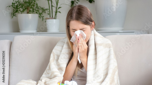 Portrait of sick woman sneezing in paper tissue on sofa