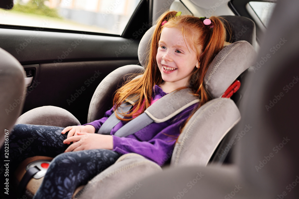 baby little red-haired girl smiling while sitting in a child car seat. Safe transportation of children in the car. baby little red-haired girl smiling while sitting in a child car seat. Safe transportation of children in the car.